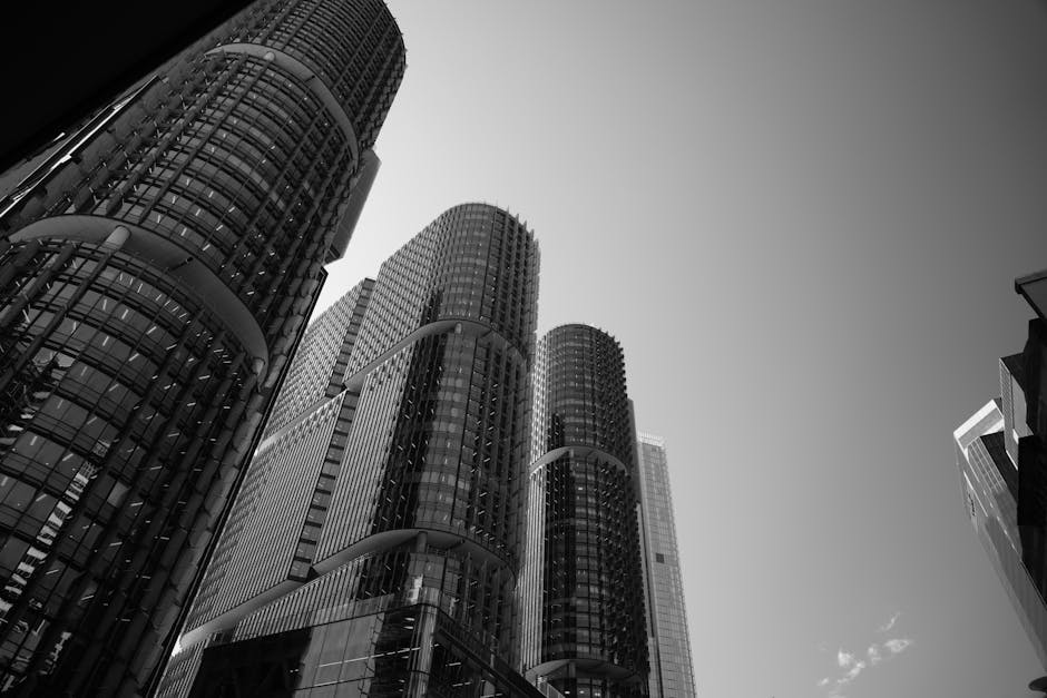 Dramatic black and white photograph of modern skyscrapers under a clear sky.